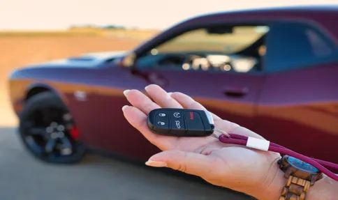 Digitaleanmeldung - Kfz Zulassungsdienst - Nahaufnahme einer Hand mit einem modernen Funkschlüssel für Autos; im Hintergrund ist ein lila Sportwagen verschwommen zu sehen.